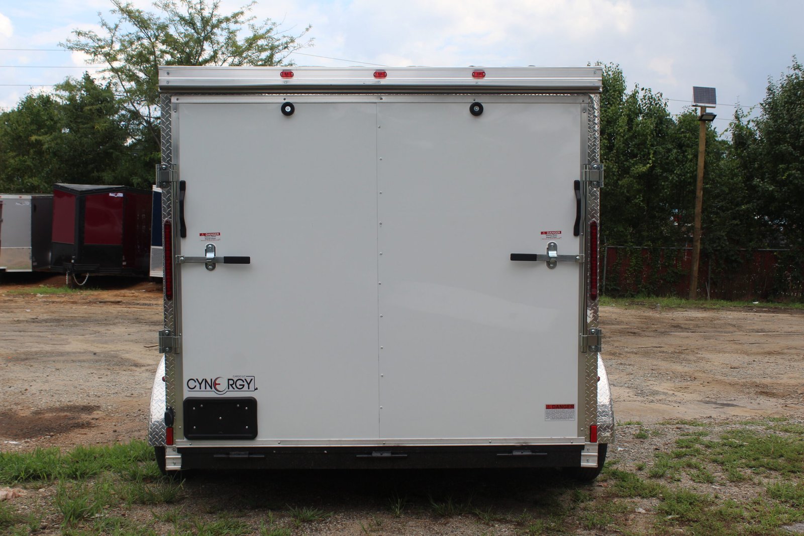 Rear view of a white Cynergy enclosed cargo trailer featuring double barn-style doors, metal trim, and secure locking latches.